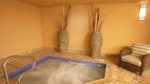 Un cuarto de spa con un jacuzzi, dos jarrones decorativos, una silla de mimbre y piso de baldosas.