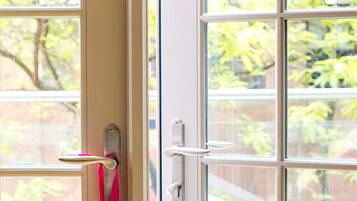 A door with a metal handle and a pink ribbon tied to it, with a window behind showing greenery outside.