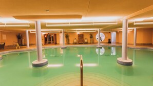 Una piscina interior con agua cristalina, rodeada de pilares blancos y suelo de baldosas.