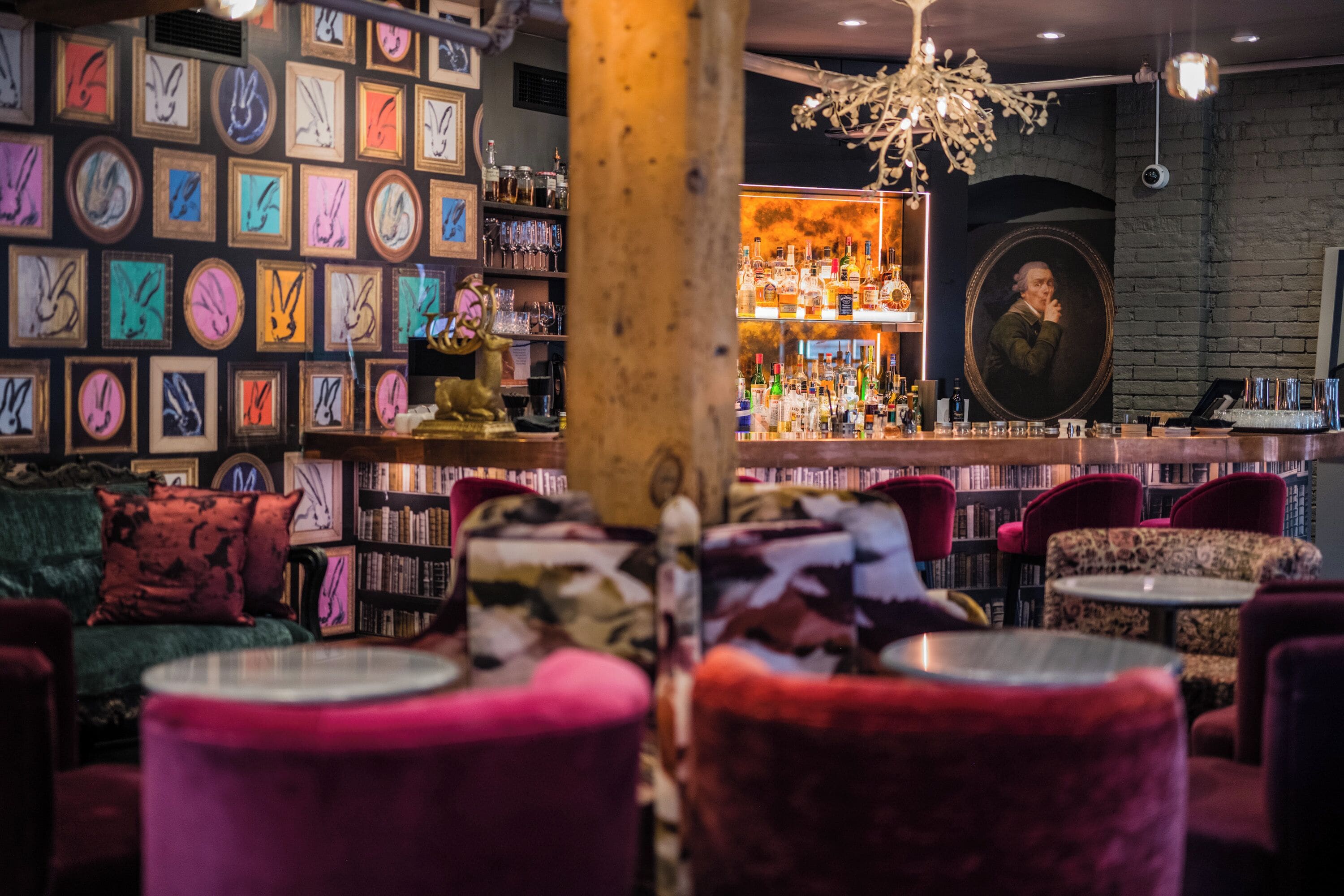 Zona de bar con diversas obras de arte enmarcadas en las paredes, una barra con botellas y un cómodo mobiliario rojo.