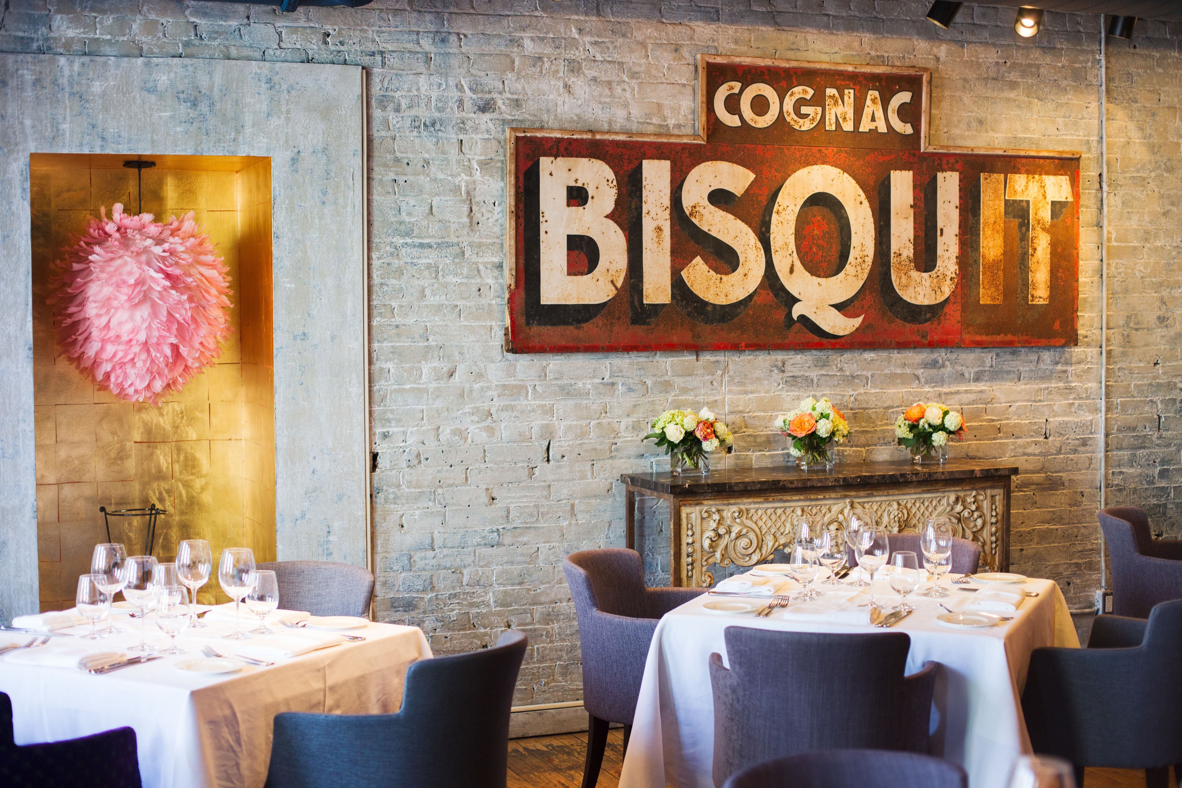 A restaurant interior with a rustic brick wall, a large sign reading "Cognac Biscuit", and tables set for dining.