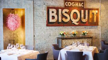 A restaurant interior with a rustic brick wall, a large sign reading "Cognac Biscuit", and tables set for dining.