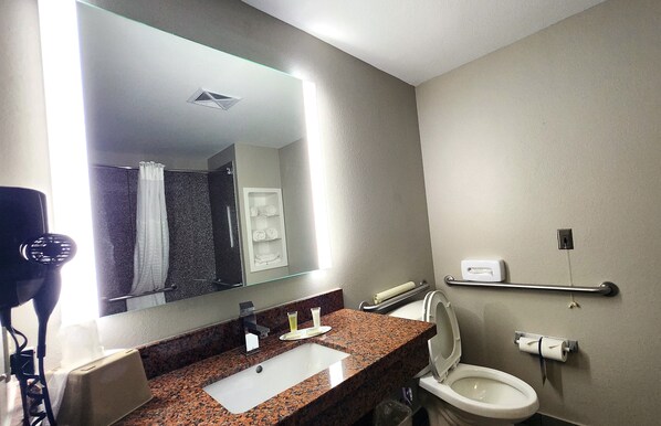 A bathroom with a granite countertop sink, a mirror, a toilet, and a towel rack.