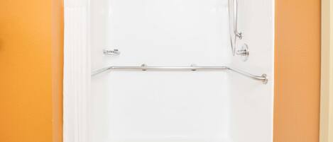 A white bathtub with a showerhead and grab bar, set against an orange wall.