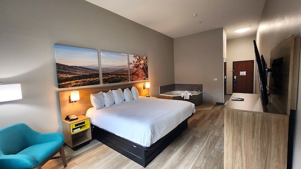 A hotel room with a large bed, a nightstand, a chair, a bathtub, and a painting of a landscape.