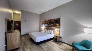 A hotel room with a bed, bedside tables, a desk, a chair, and a wall-mounted artwork.