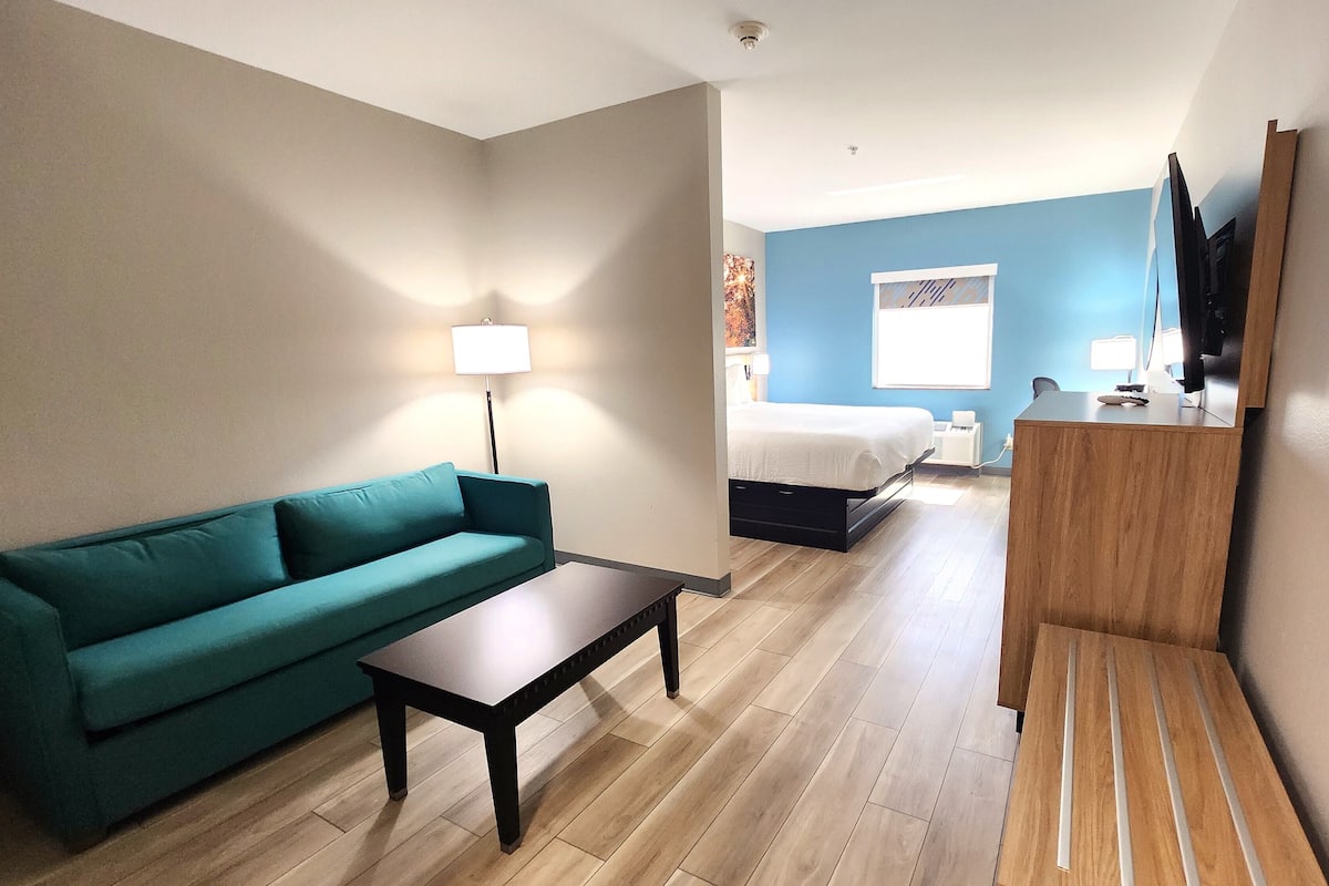 Una habitación de hotel con sofá color turquesa, una mesa de centro de madera, un escritorio con espejo, una cama y un televisor.