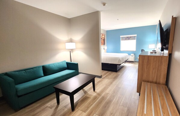 Una habitación de hotel con sofá color turquesa, una mesa de centro de madera, un escritorio con espejo, una cama y un televisor.