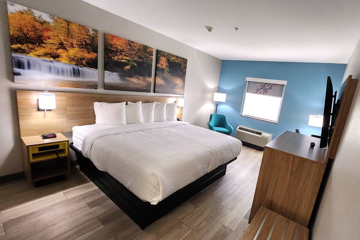 Una habitación de hotel con una cama grande, una mesita de noche de madera, un escritorio y una silla. Hay lámparas de pared y una ventana con persianas.