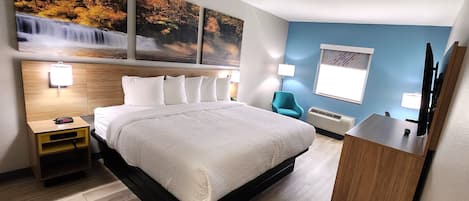 Una habitación de hotel con una cama grande, una mesita de noche de madera, un escritorio y una silla. Hay lámparas de pared y una ventana con persianas.