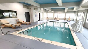 An indoor swimming pool with lounge chairs, a covered area, and clear poolside markings.