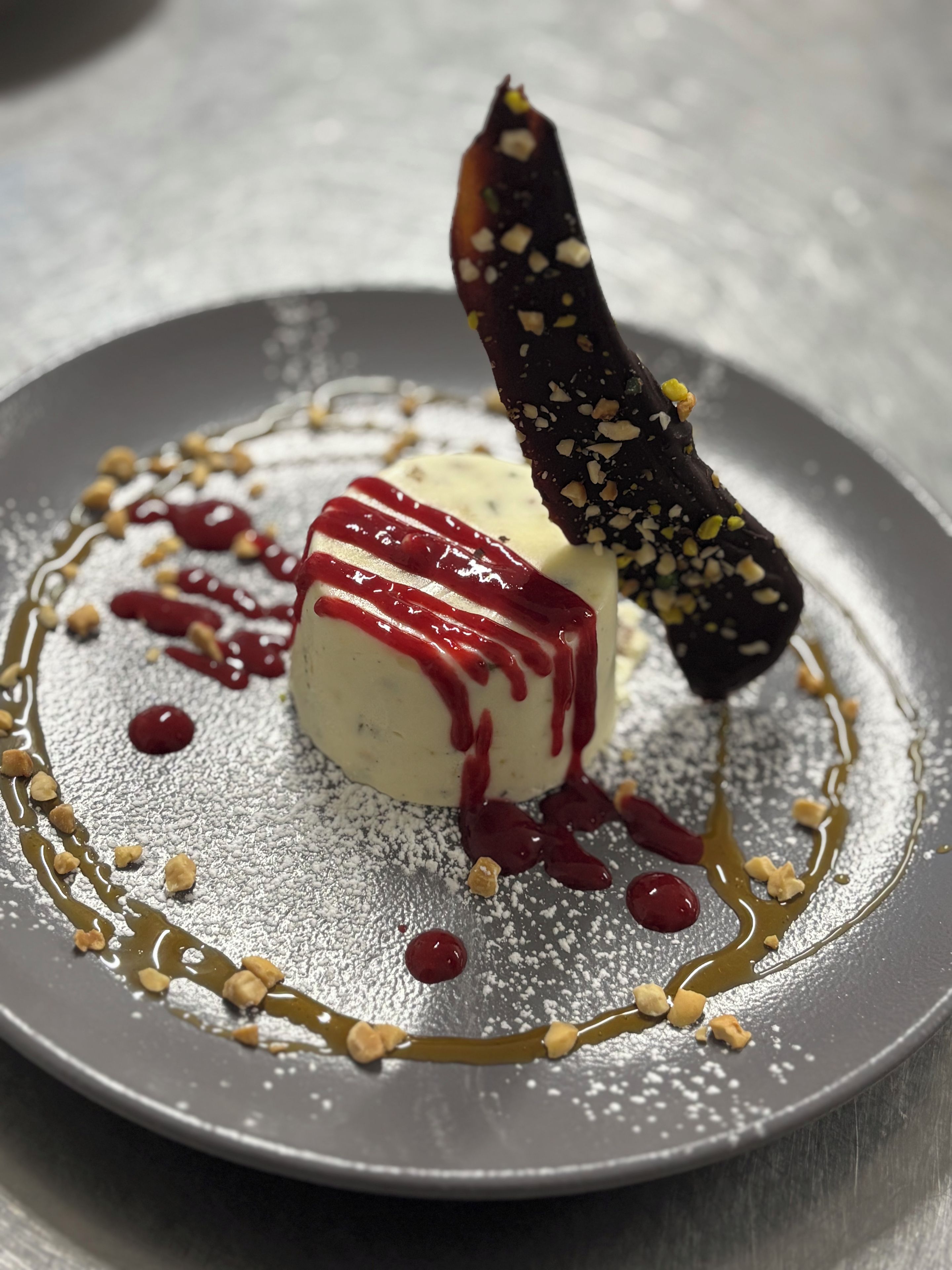 Un postre en un plato con azúcar glas, hilos de sirope y nueces.