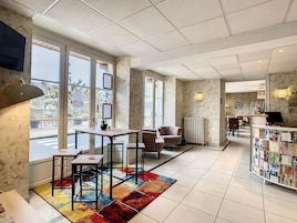 Un moderno vestíbulo de hotel con un área de estar central, ventanas amplias y una alfombra colorida.
