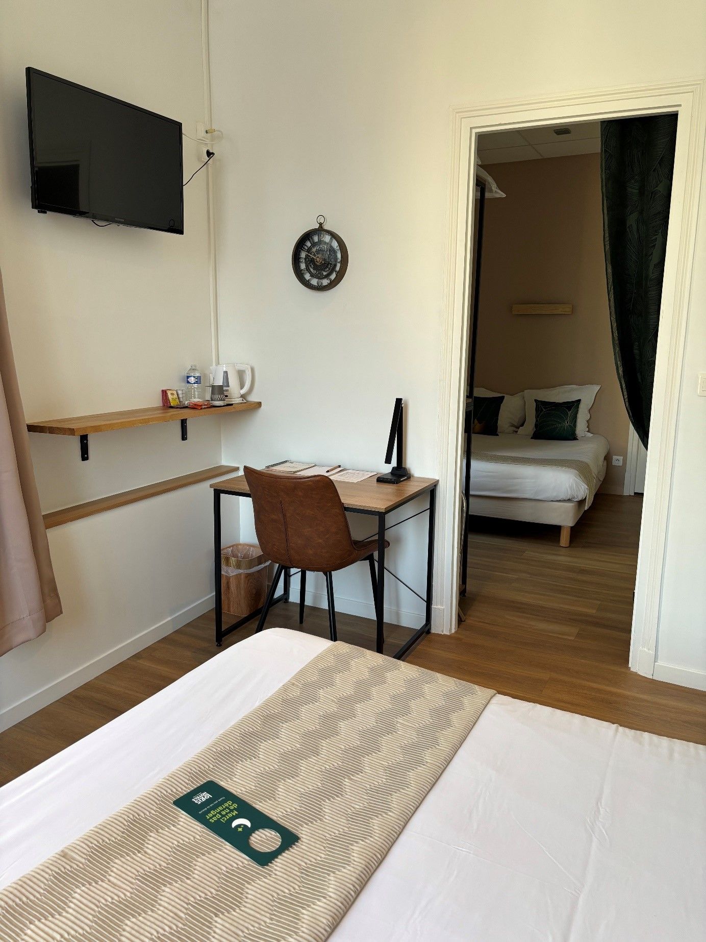 Una habitación de hotel con una cama, un escritorio con una silla, un televisor montado en la pared y una puerta que da a otra habitación.
