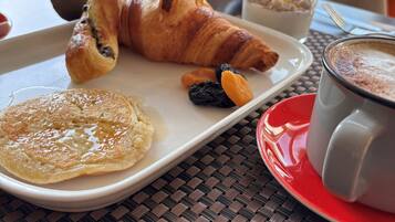 Un plato de desayuno con cruasanes, un panqueque y frutas secas, junto con un vaso de jugo de naranja y una taza de café.