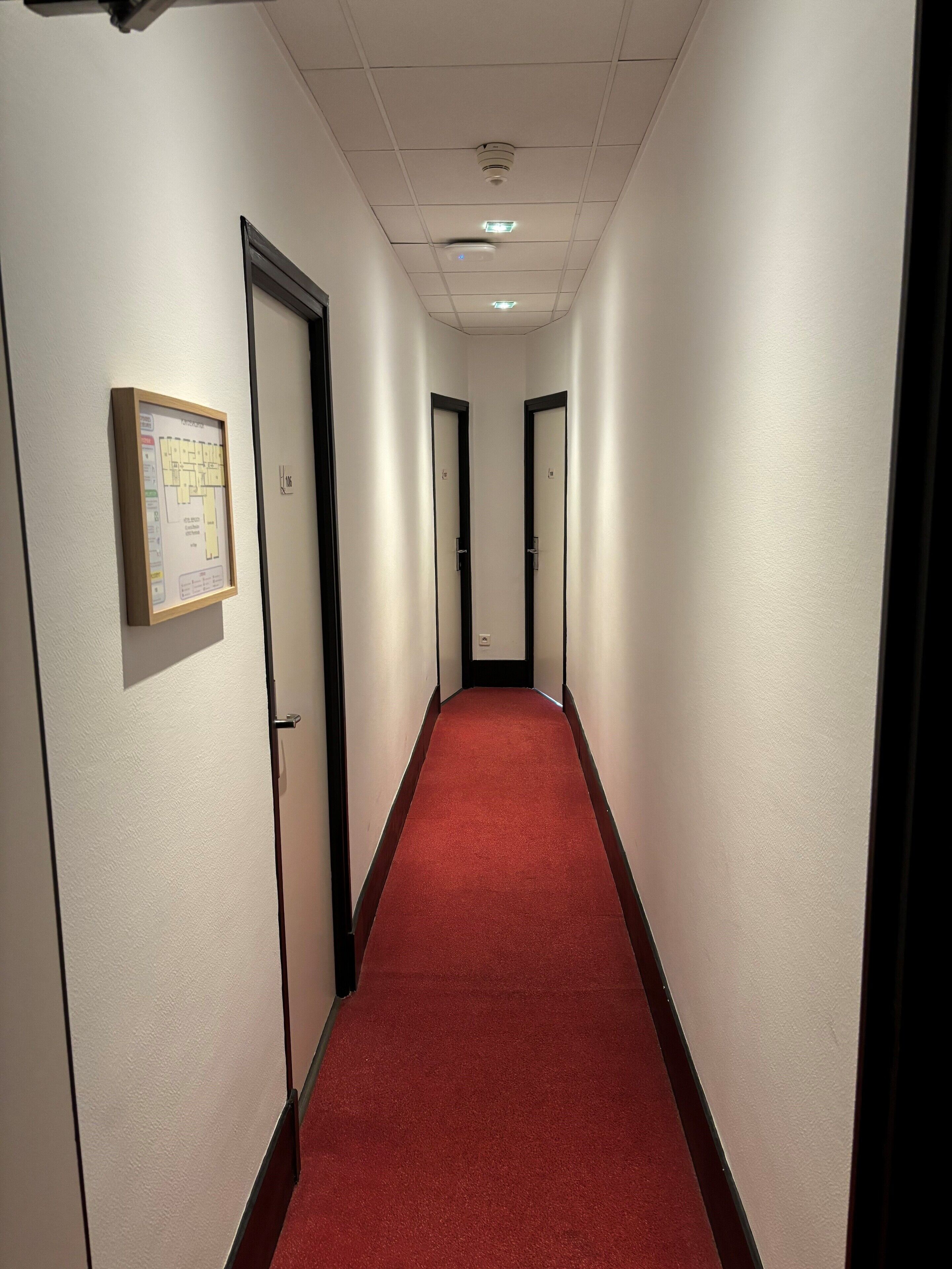 A hallway with a red carpet, white walls, and doors with black frames.