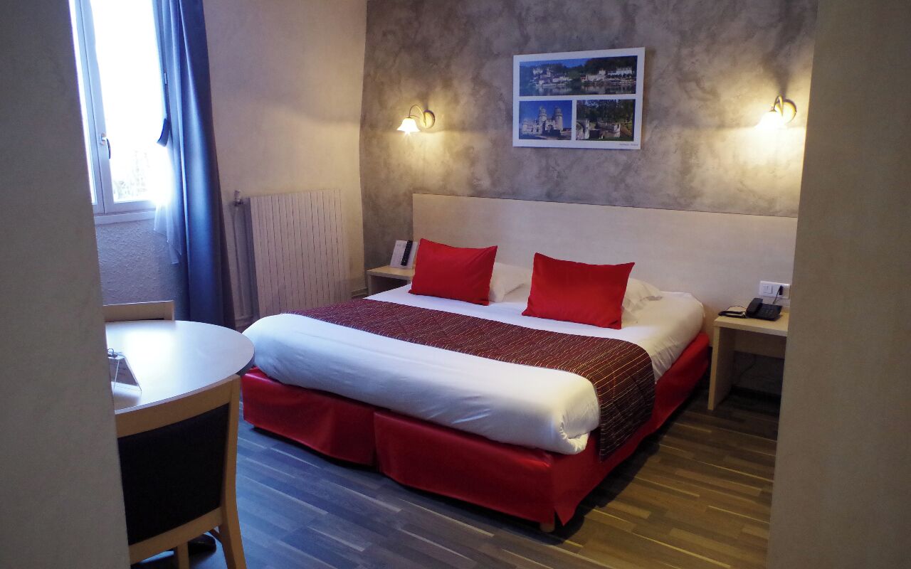 A hotel room with a large bed, two bedside tables, a small table, and a view of the outdoors.