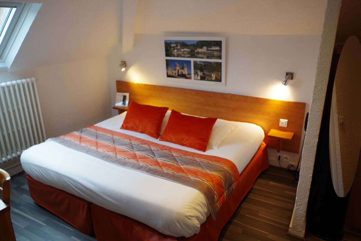 Ett hotellrum med en stor säng, en sänggavel, två sänglampor, ett element och en inramad tavla på väggen.