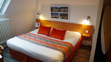 A hotel room with a large bed, a headboard, two bedside lamps, a radiator, and a framed picture on the wall.