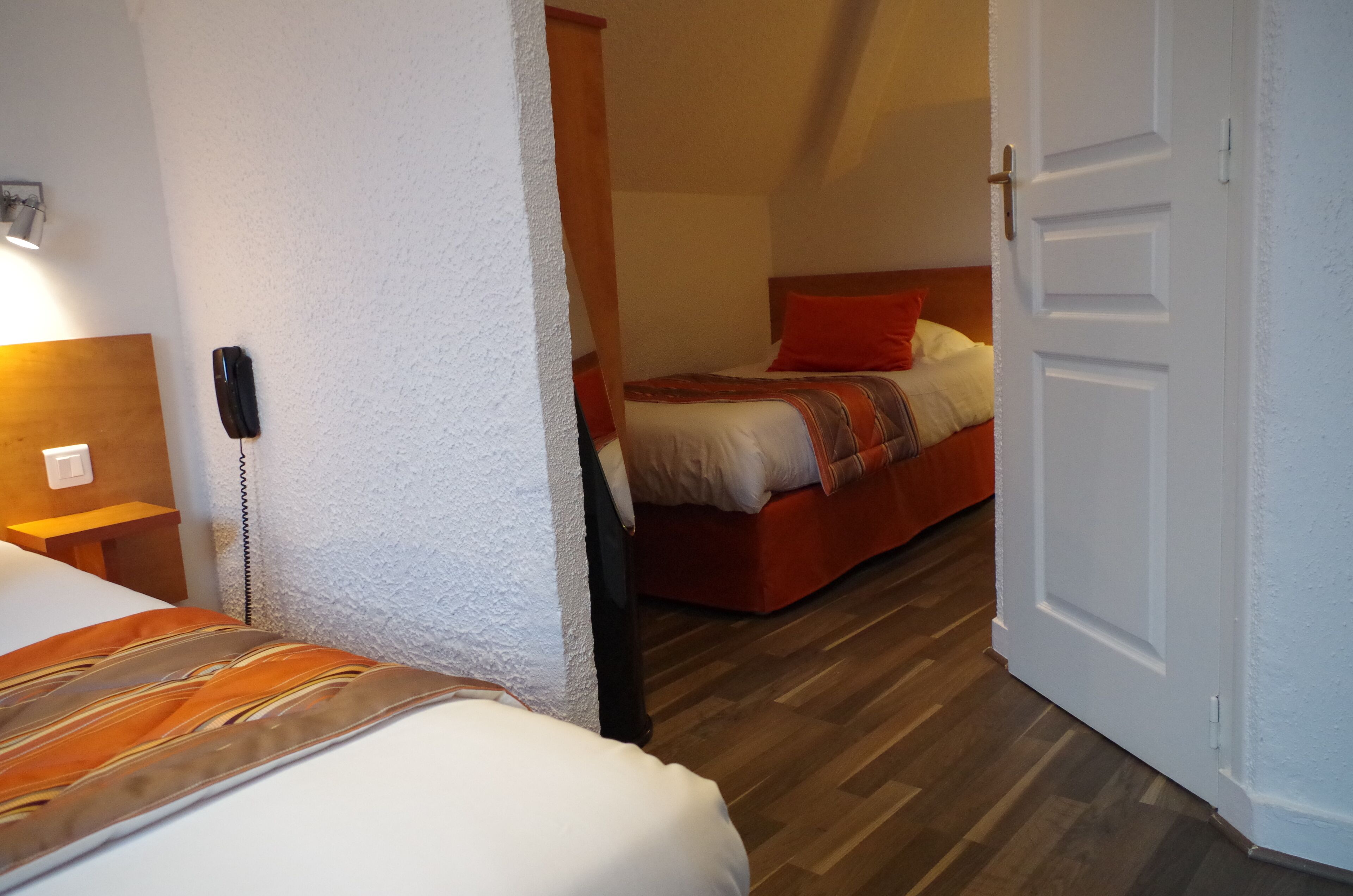Een hotelkamer met een bed, nachtkastje, telefoon en een deur naar een andere kamer.