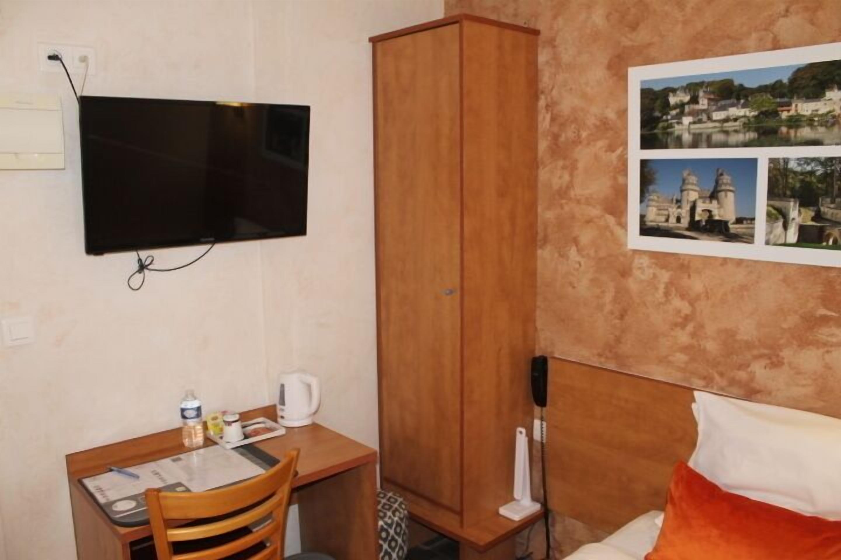 A room with a bed, a desk with a chair, a television mounted on the wall, and a wardrobe.