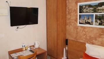A room with a bed, a desk with a chair, a television mounted on the wall, and a wardrobe.