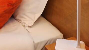 Een hotelkamer met een bed, een witte nachtkastje, een afstandsbediening en een witte lamp.