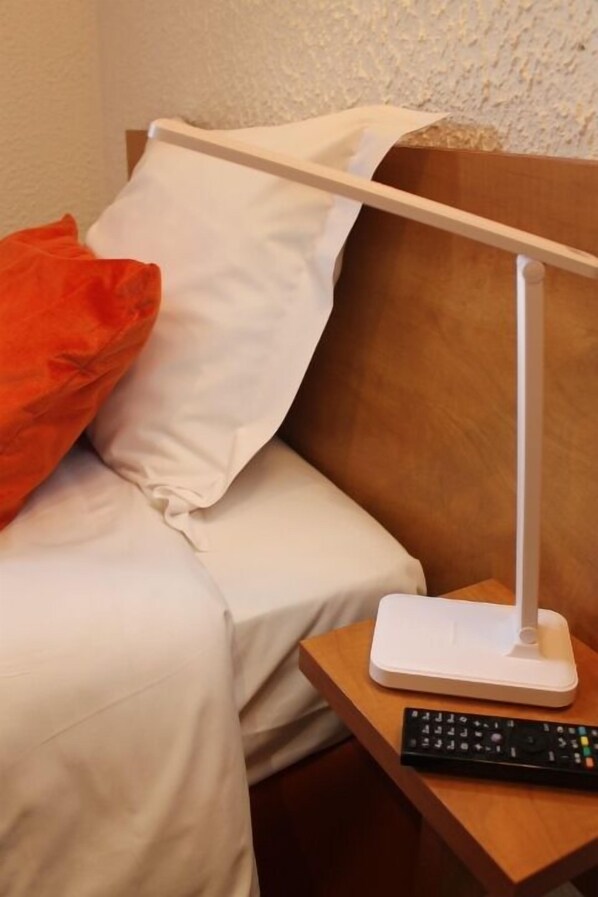 Una habitación de hotel con una cama, una mesita de noche blanca, un control remoto y una lámpara blanca.