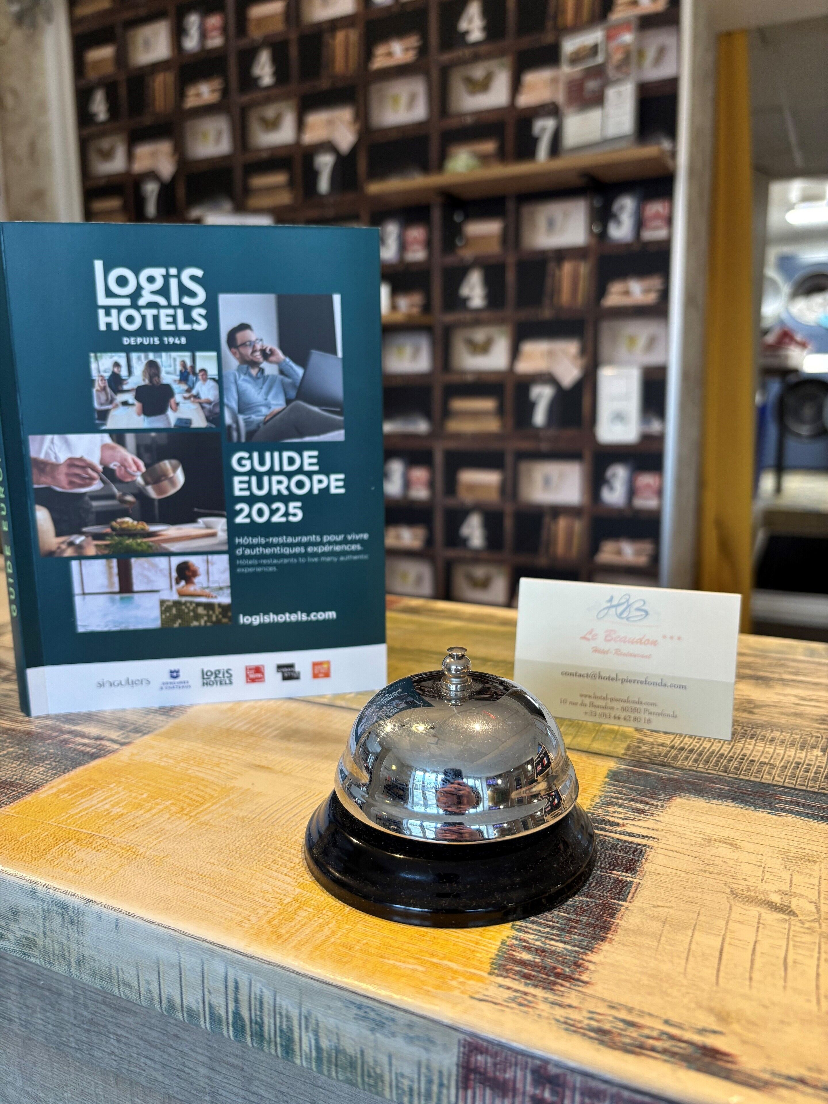 Zona de recepción de un hotel con un expositor de folletos, una mesa de recepción y una pared de cuadros enmarcados.