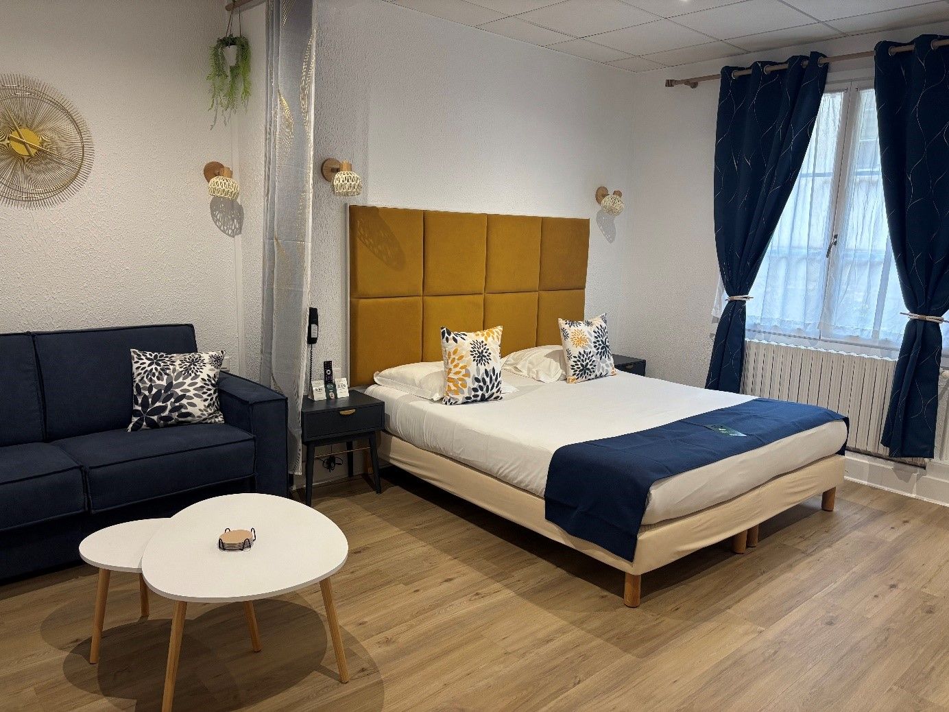 A hotel room with a bed, a sofa, a small table, and a window with curtains.