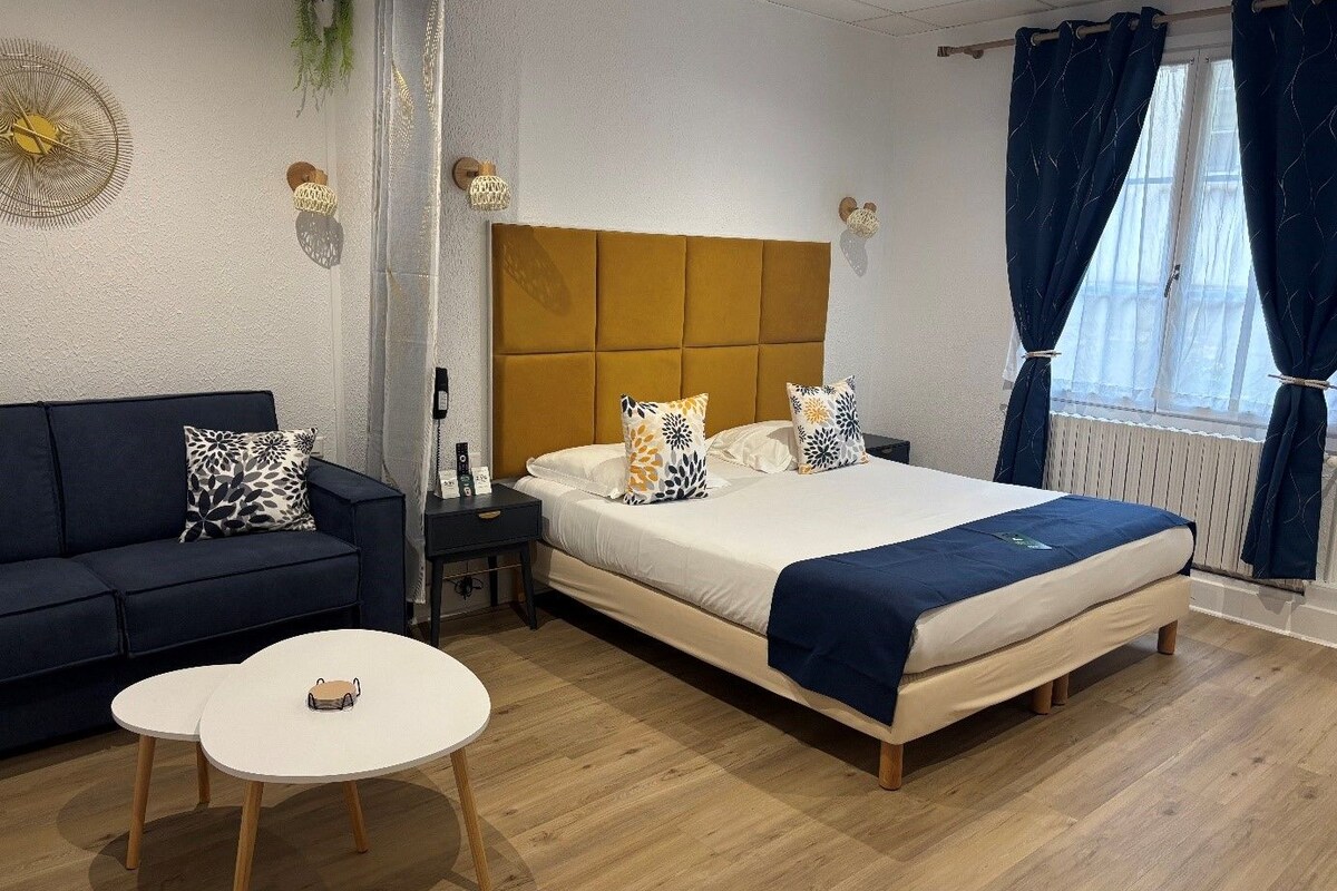 Una habitación de hotel con cama, sofá, una mesita y ventana con cortinas.