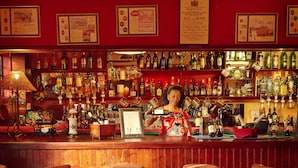A bar area with wicker chairs, a wooden table, and a variety of bottles and glasses. - The Foresters Arms (Mhlambanyatsi)