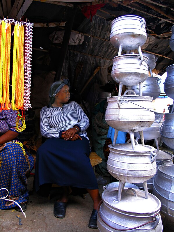 A person seated in a rustic setting with metal containers stacked around them. - The Foresters Arms (Mhlambanyatsi)
