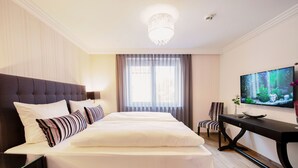 A hotel room with a large bed, a television, a desk, and a chair.