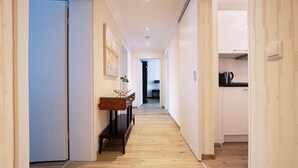 A narrow hallway with wooden flooring, a bench, and a small table with a vase.