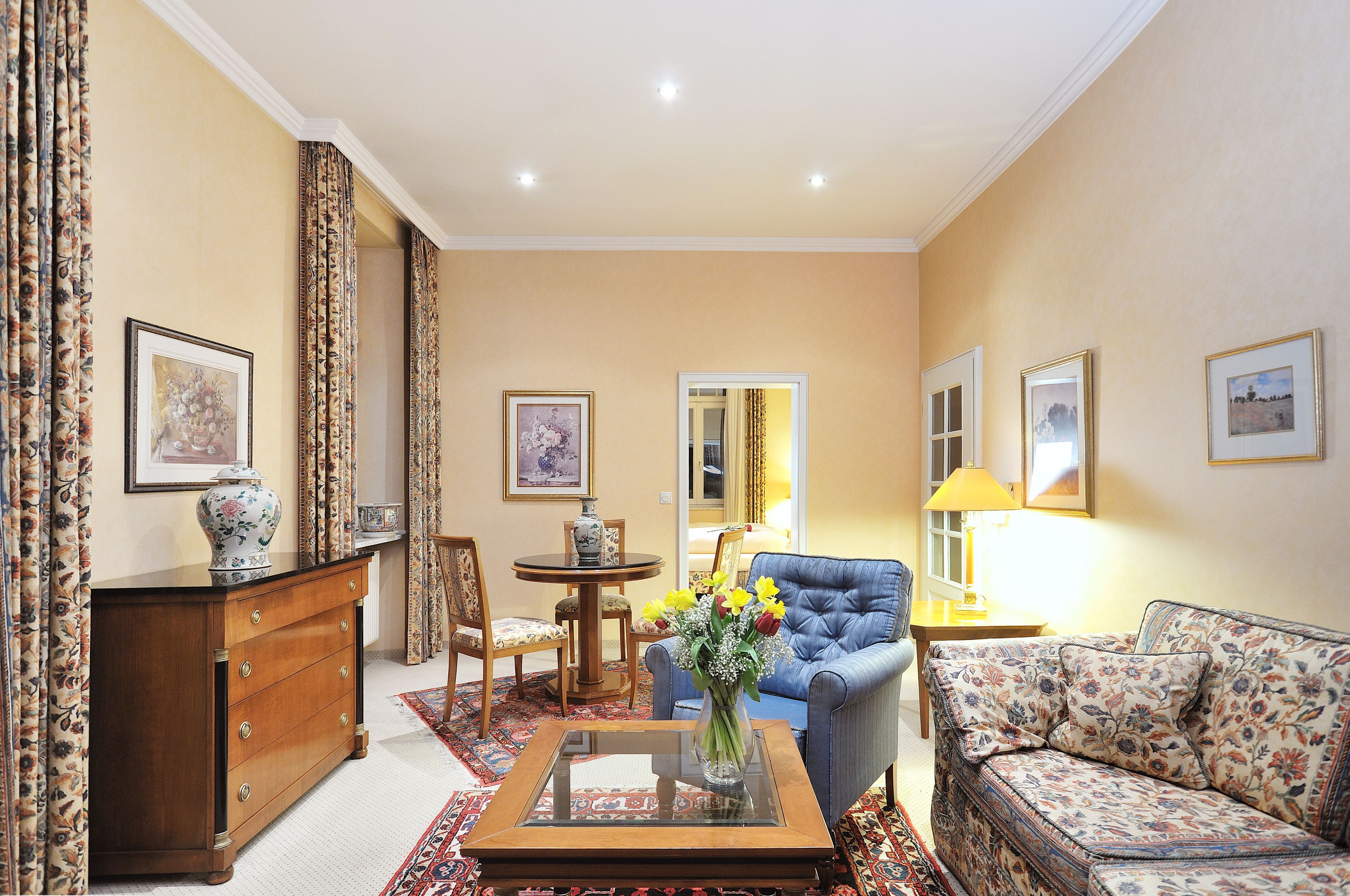 Ein Wohnzimmer mit Sofa, Couchtisch mit Blumenvase, Holzschrank, Sessel und Lampe.