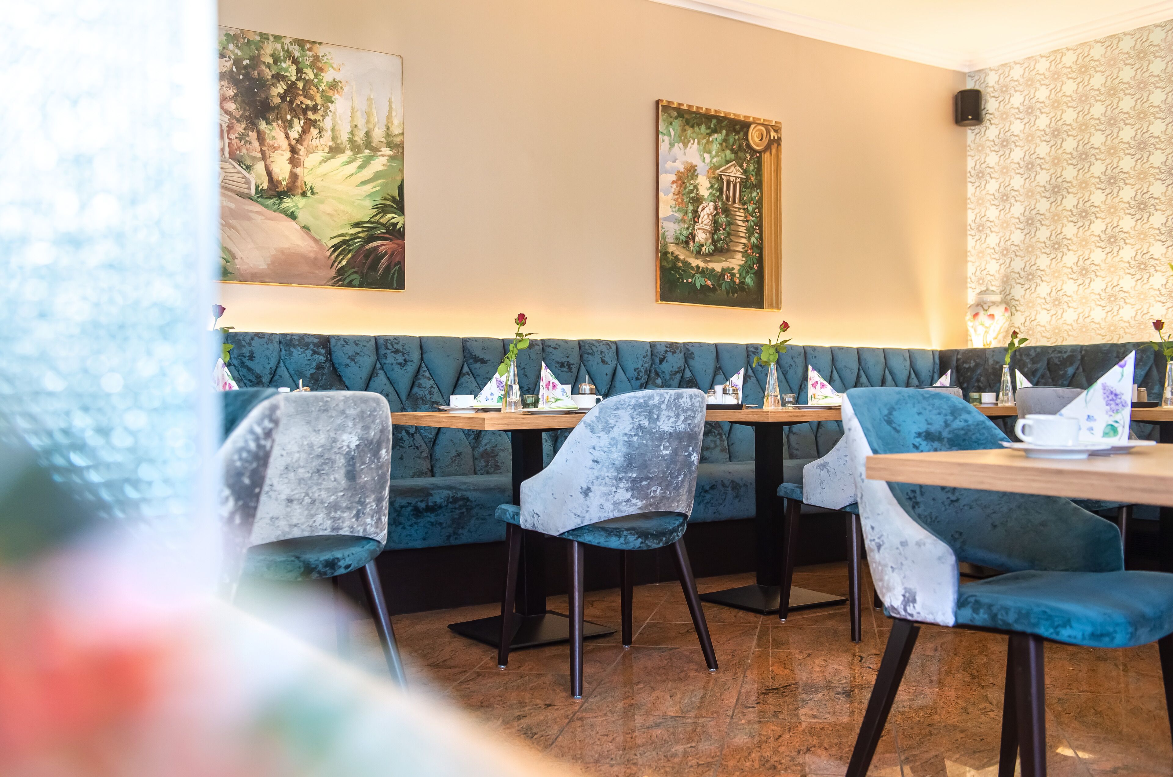 Een restaurantinterieur met blauwe gestoffeerde zitplaatsen, houten tafels en bloemrijke wanddecoratie.