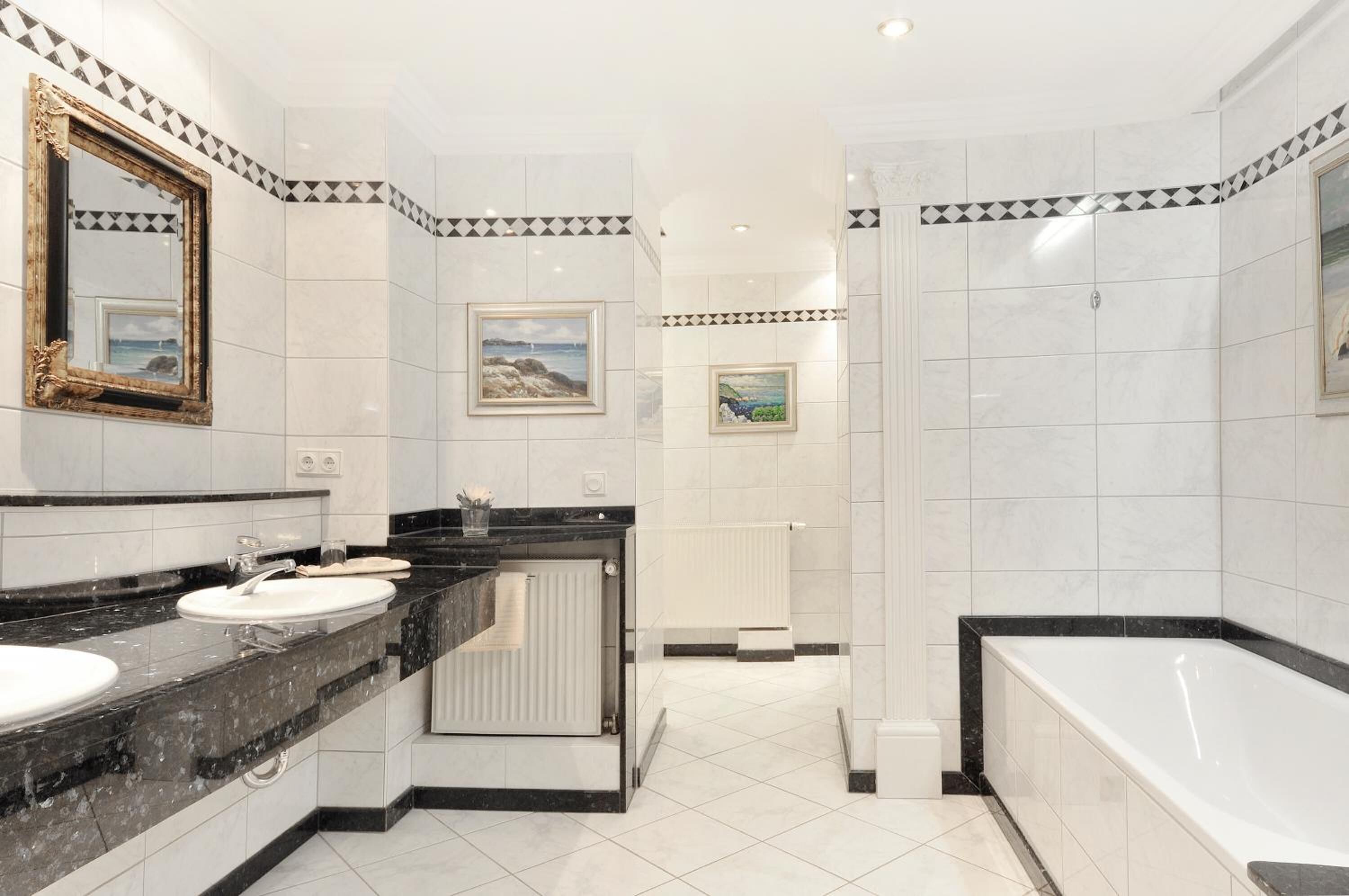 A modern bathroom with a black and white tiled design, a large mirror, two sinks, a bathtub, and a shower area.