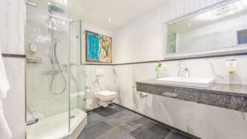 A modern bathroom with a glass-enclosed shower, a white toilet, a marble sink, and a large mirror.