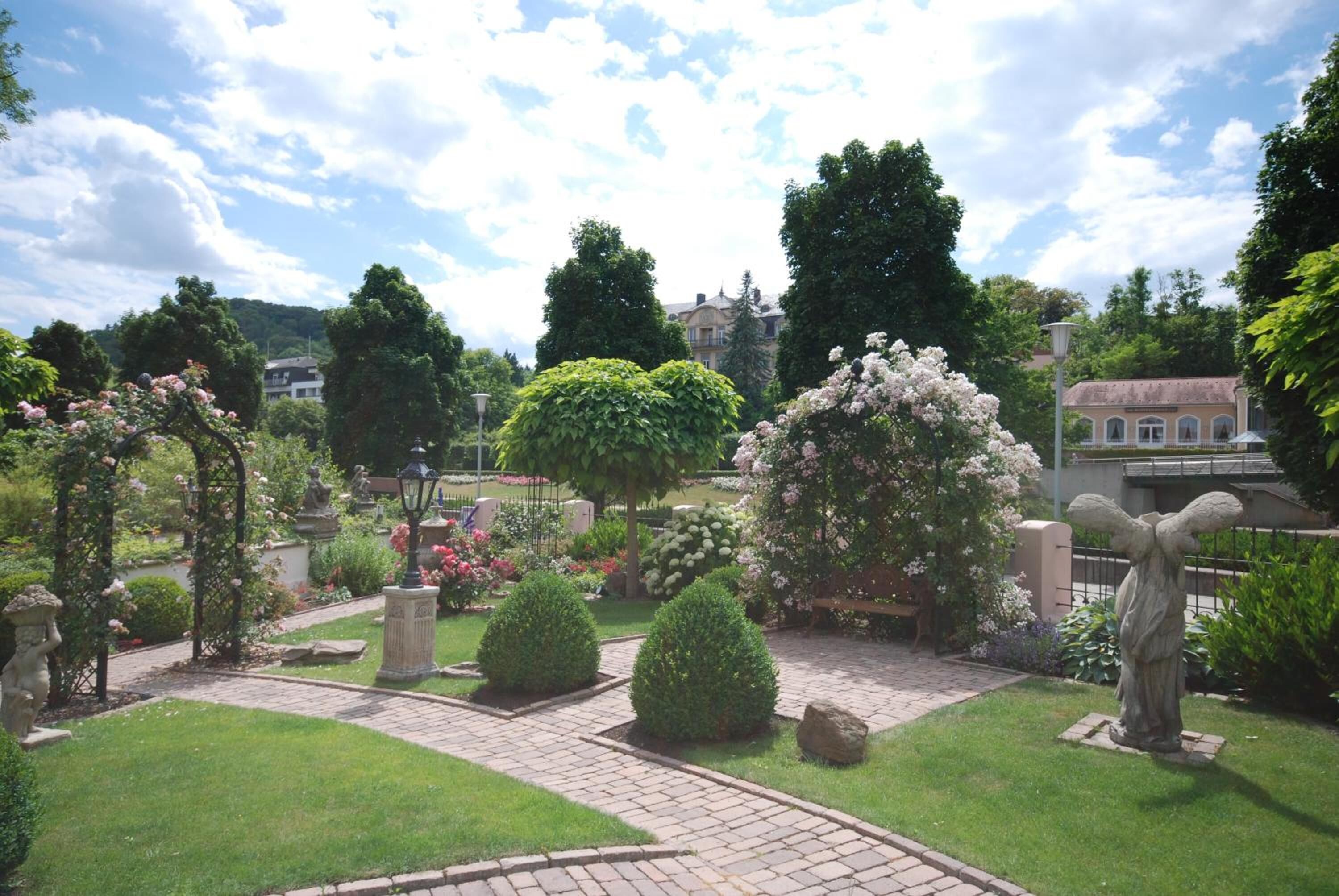 Ein gepflegter Garten mit einem gepflasterten Weg, verschiedenen Sträuchern und einer Statue.
