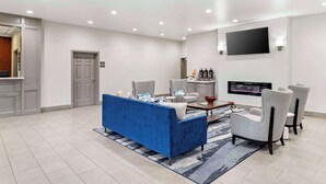 Un salon moderne avec un canapé bleu, deux fauteuils gris, une table basse et un téléviseur à écran plat fixé au mur.