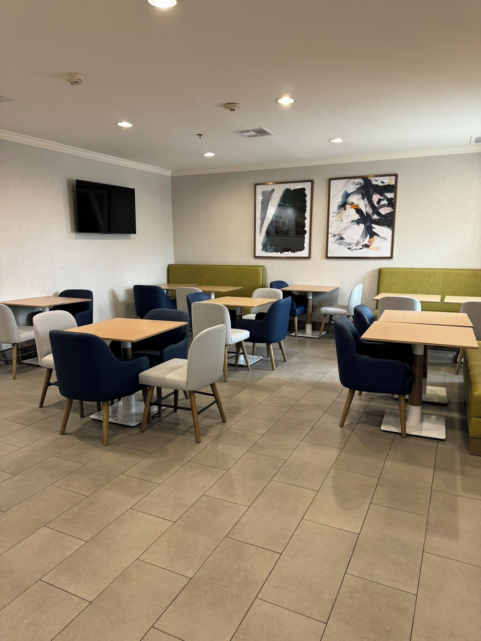 A modern dining area with tables and chairs, a flat-screen TV mounted on the wall, and two abstract paintings.