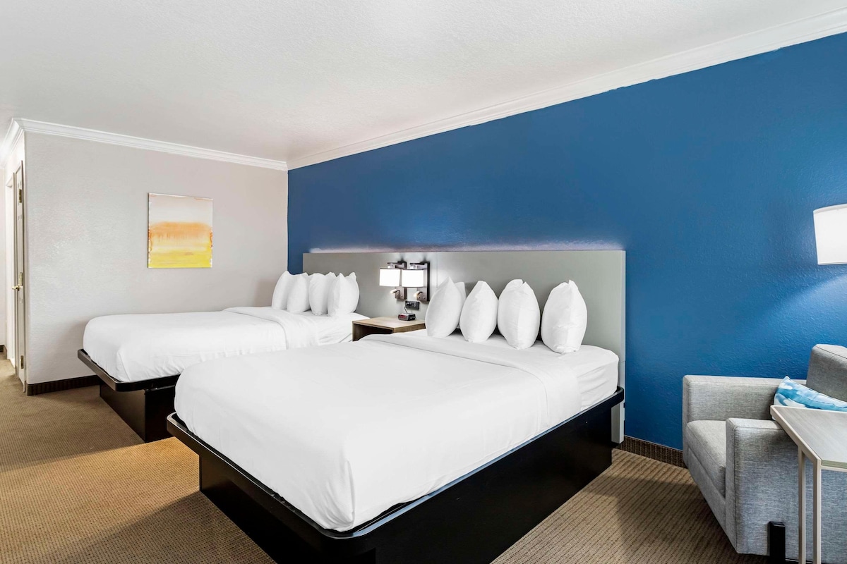 A hotel room with two beds, a desk, and a chair.