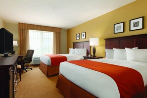 A hotel room with two beds, a desk with a computer, a chair, and a window with curtains.