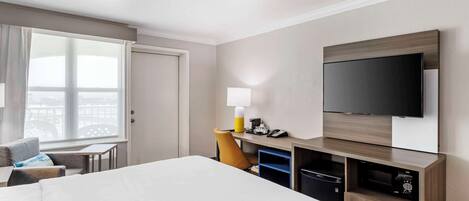 Une chambre d’hôtel avec un grand lit, un bureau avec une lampe, une télévision et une vue sur la ville par la fenêtre.