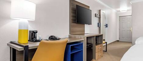 A hotel room with a desk, chair, TV, and a bed.