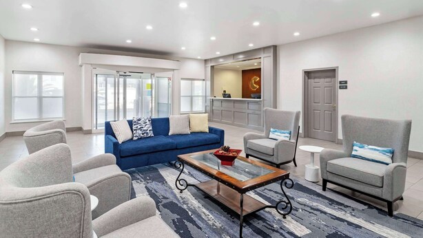 Un salon moderne avec un canapé bleu, des fauteuils gris, une table basse en verre et un tapis à motifs.