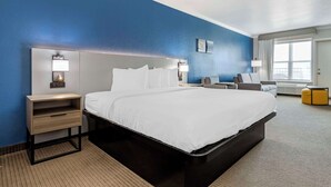 Une chambre d’hôtel moderne dotée d’un grand lit, de tables de chevet avec des lampes, d’un petit coin salon et d’une fenêtre avec des rideaux.