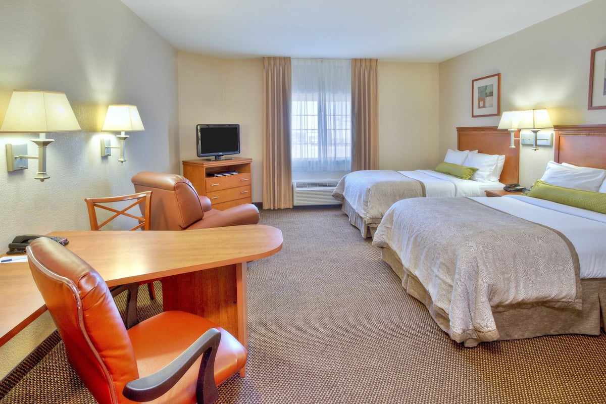 A hotel room with two beds, a desk with a chair, a TV, and two wall-mounted lamps.