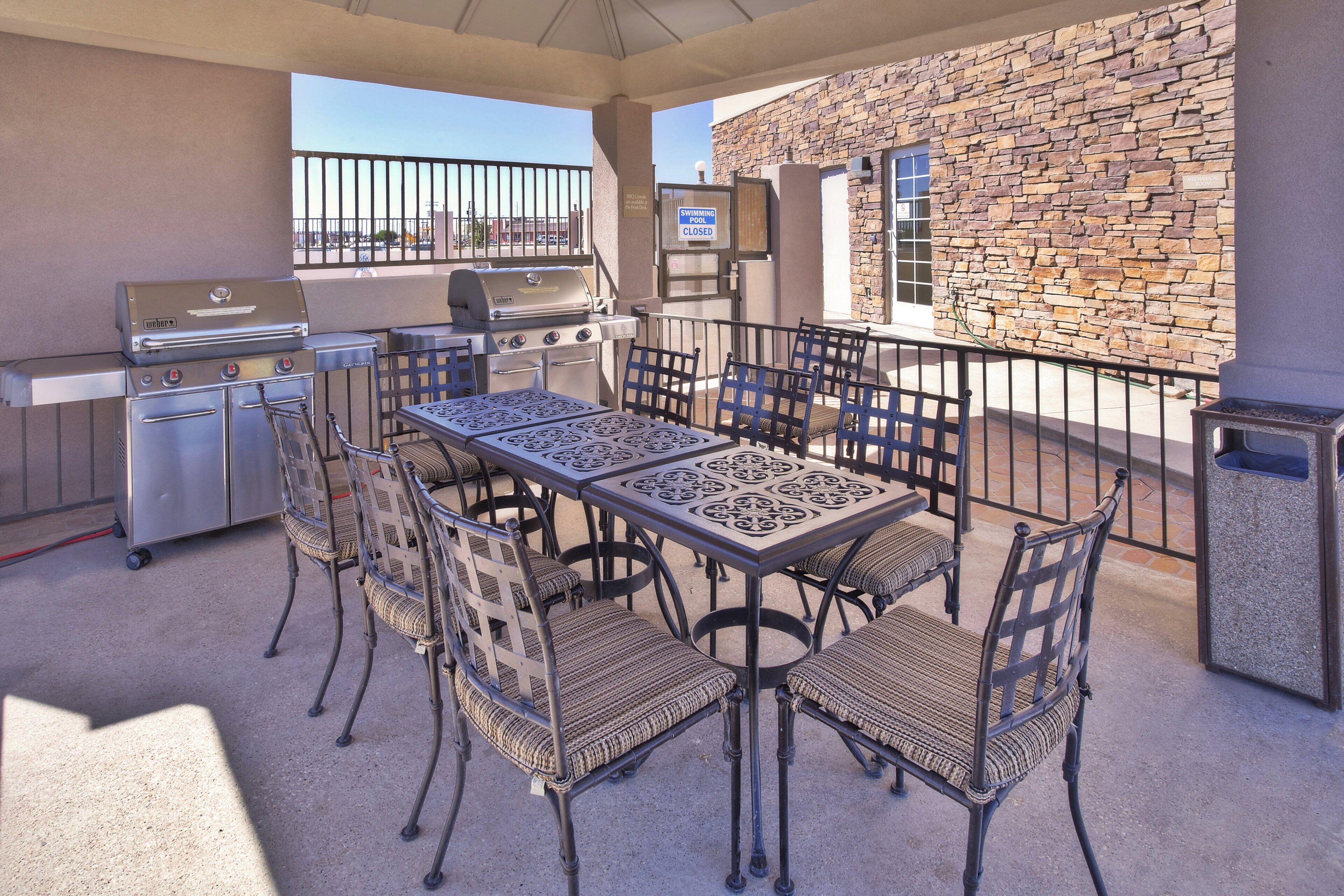 An outdoor patio with a grill, dining table, and chairs, a stone wall, and a closed swimming pool.